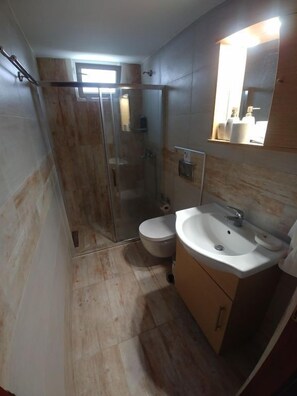 A bathroom with a glass shower enclosure, a toilet, and a sink with a mirror above it. - Dora Apartments (Zakynthos)