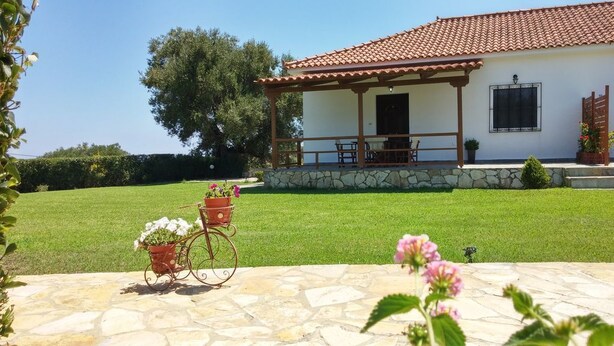 A house with a tiled roof, a stone foundation, and a covered porch with outdoor furniture. - Dora Apartments (Zakynthos)