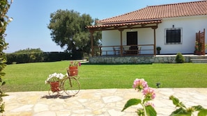 A house with a tiled roof, a stone foundation, and a covered porch with outdoor furniture. - Dora Apartments (Zakynthos)