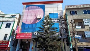 A hotel with a large blue and pink sign, multiple balconies, and various signs for services like a barber shop and a laptop store. - Hotel Champion Inn near Yeswantpur Junction Railway Station (Bengaluru)