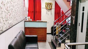 A hotel lobby with a reception desk, a black leather sofa, a staircase with red railings, and a patterned wallpaper wall. - Hotel Champion Inn near Yeswantpur Junction Railway Station (Bengaluru)
