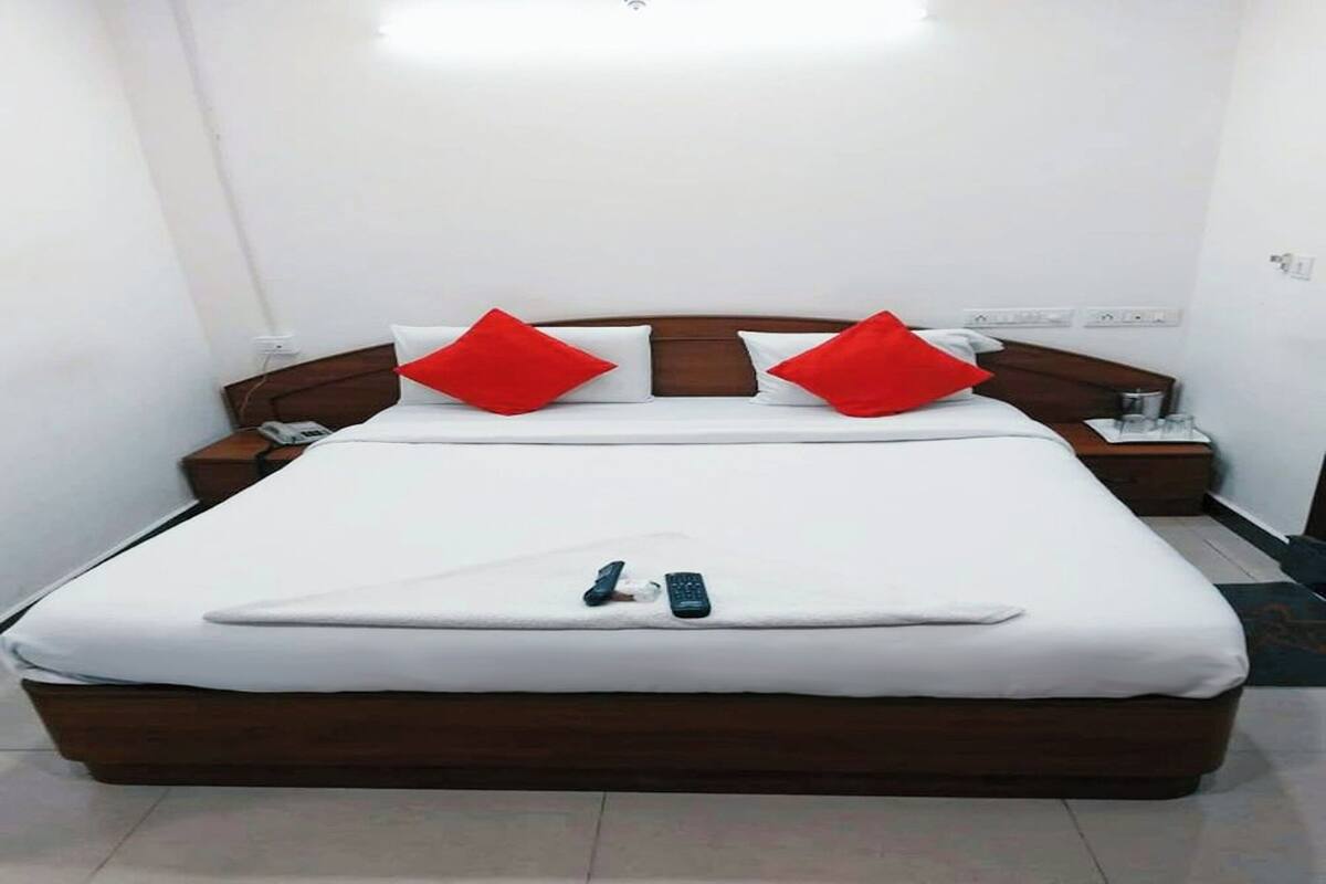 A neatly made bed with white bedding and red pillows, a bedside table with a lamp, and a remote control on the bed.