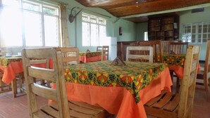 A dining area with wooden tables and chairs, covered with orange tablecloths. - Fort Coleb Guest House (Mbarara)