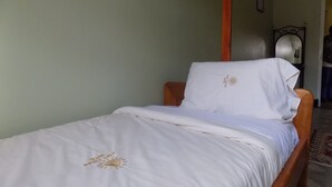 A single bed with a white bedspread and pillow, a wooden headboard, and a plain wall. - Fort Coleb Guest House (Mbarara)