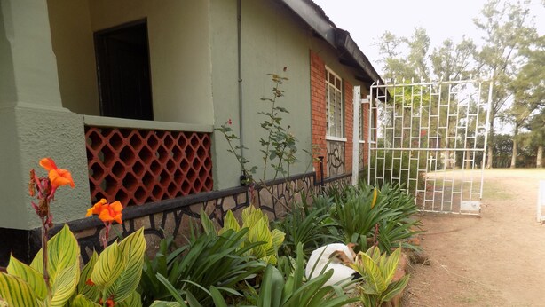 A house with a fenced yard, green plants, and a white gate. - Fort Coleb Guest House (Mbarara)