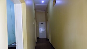 A narrow hallway with cream-colored walls and a brown carpet. A door is visible at the end of the hallway. - Fort Coleb Guest House (Mbarara)