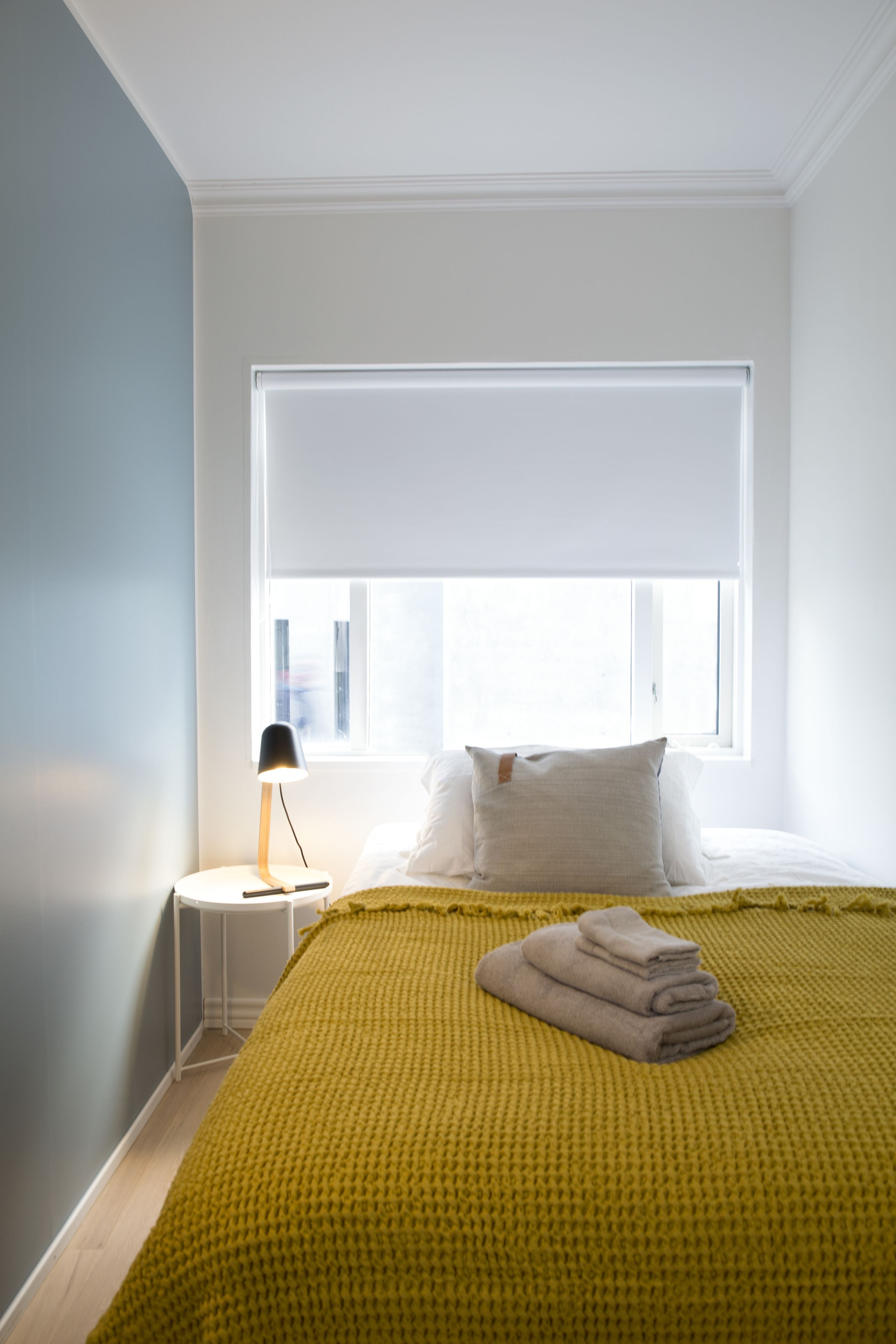 A bedroom with a bed, a bedside lamp, a window, and a yellow knitted blanket.