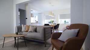 A modern living room with a sofa, armchair, coffee table, and dining area with chairs and a table. - Apartment T10c (Reykjavik)