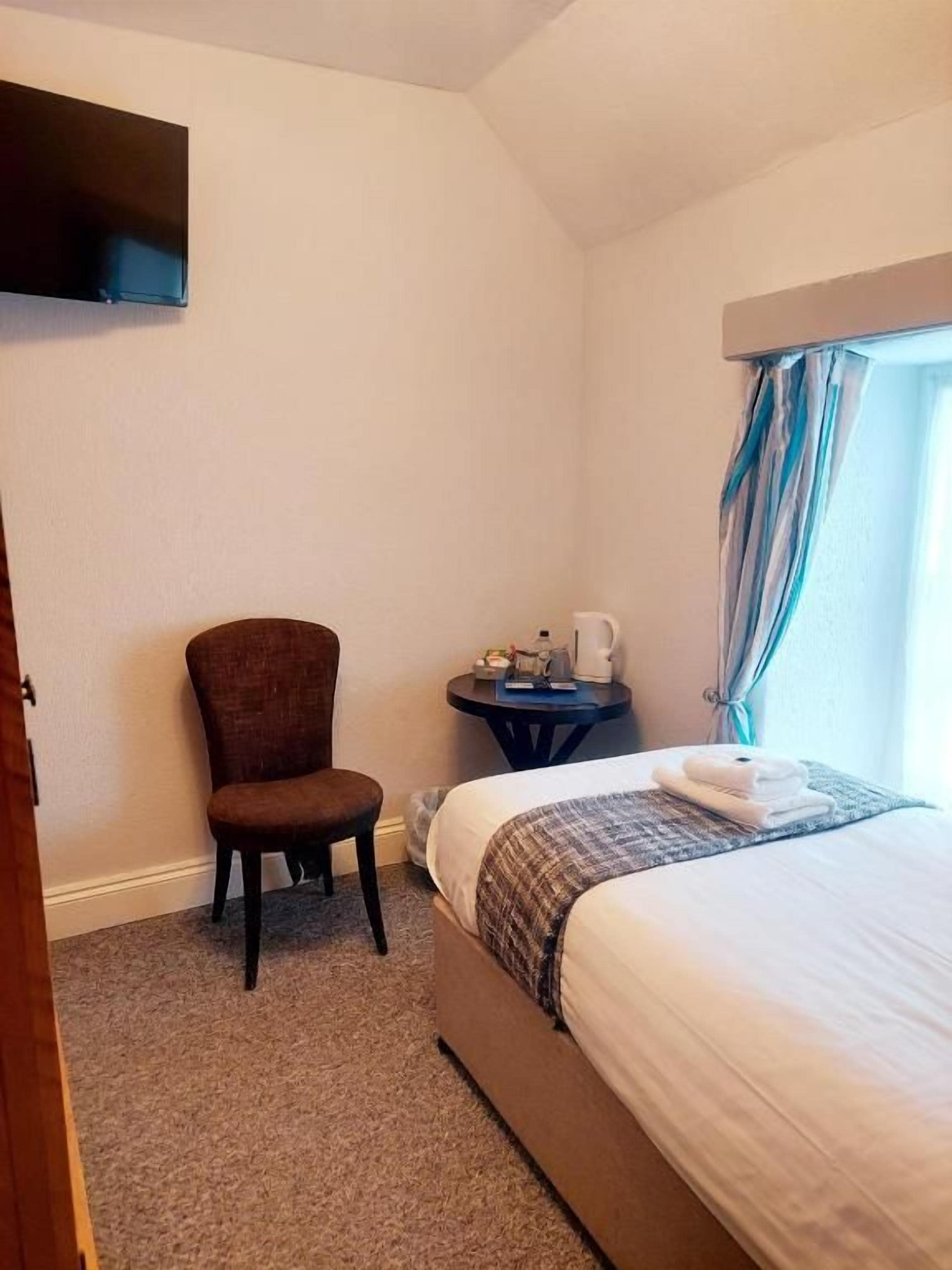 A hotel room with a bed, a chair, a small table with a coffee maker, and a television mounted on the wall.