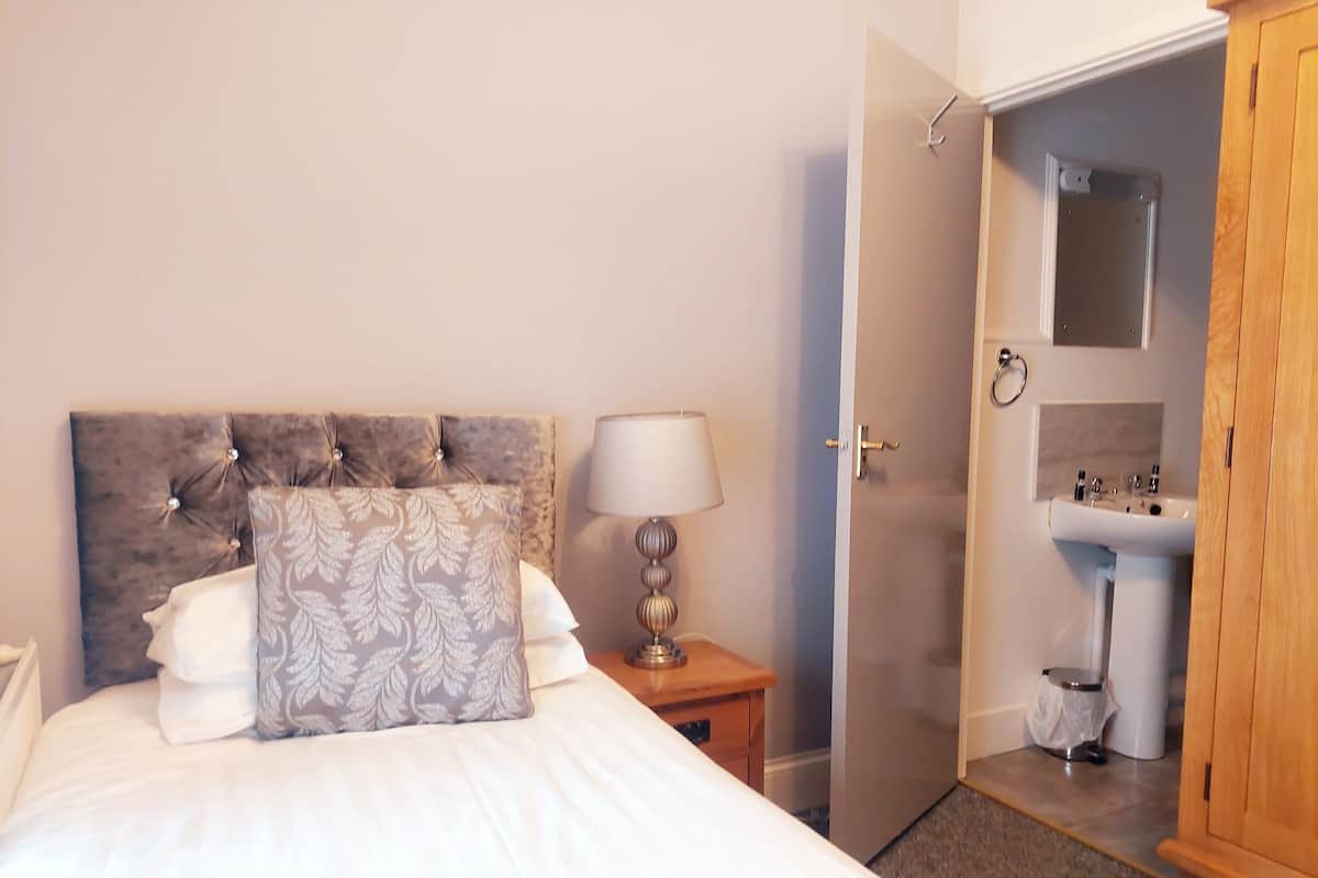 A bedroom with a bed, bedside lamp, and a bathroom visible through an open door.