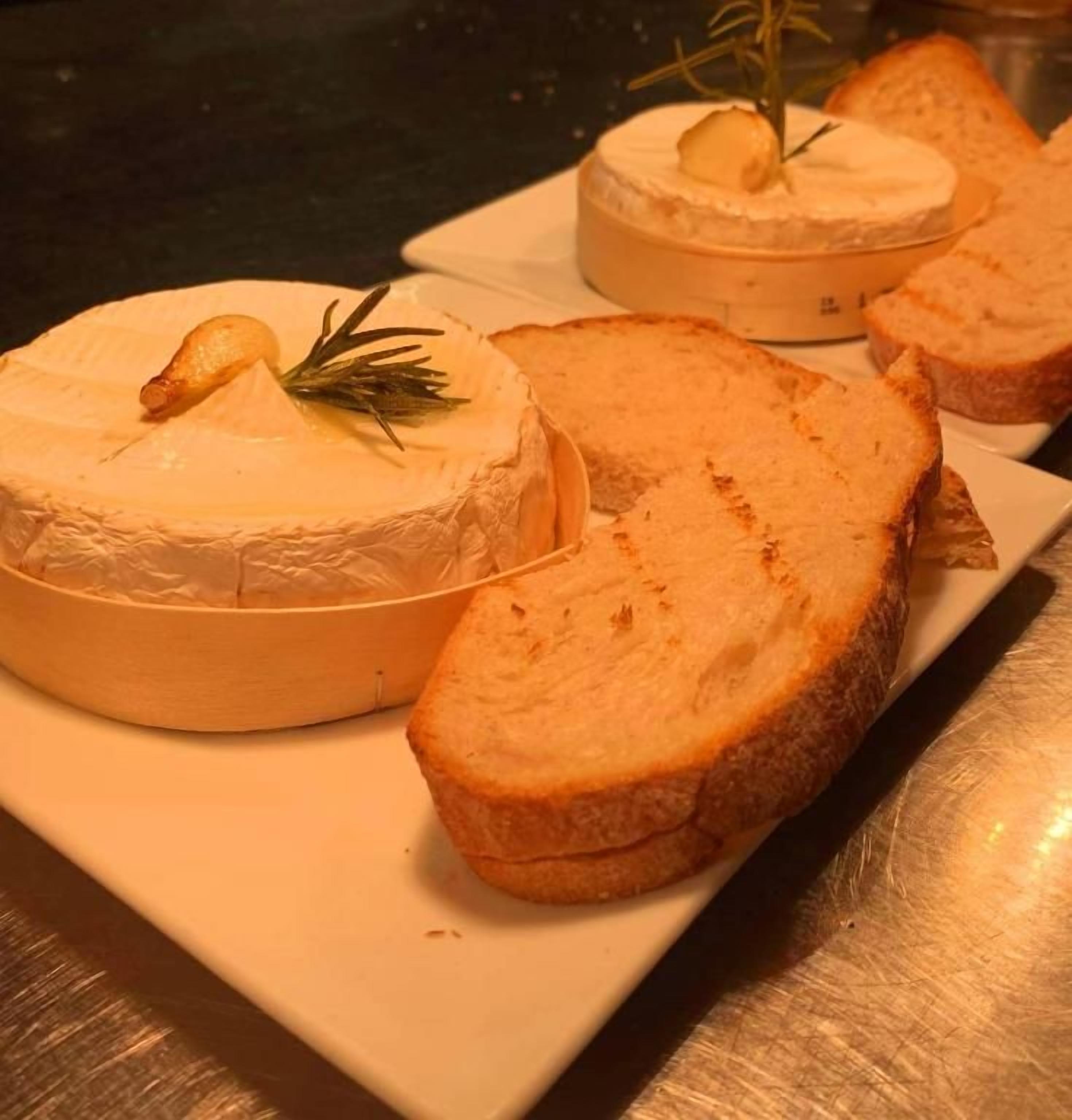 Un queso redondo con un adorno encima, acompañado de rebanadas de pan sobre un plato blanco.