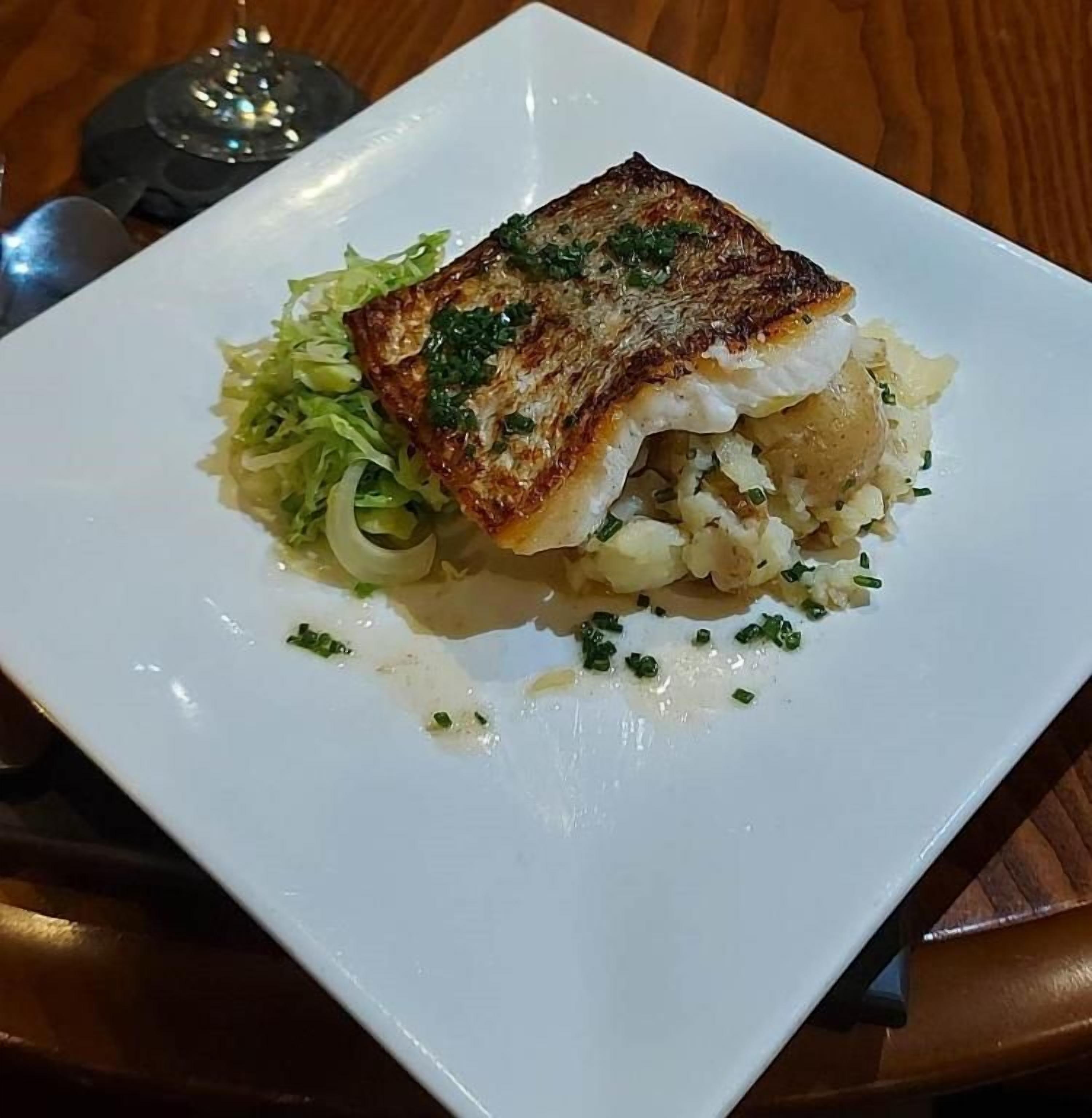 Une assiette blanche contenant un morceau de poisson grillé, des pommes de terre et une portion de légumes verts.