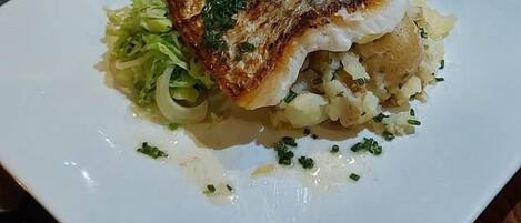 A white plate with a piece of grilled fish, some potatoes, and a side of green vegetables.