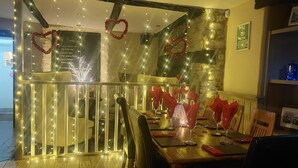 A dining area with a wooden table set for two, a glass partition with heart-shaped decorations, and a stone wall in the background. - The Black Lion Royal Hotel (Lampeter)