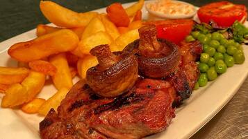 Un plato con filete a la parrilla, papas fritas, champiñones, guisantes y una rodaja de tomate.