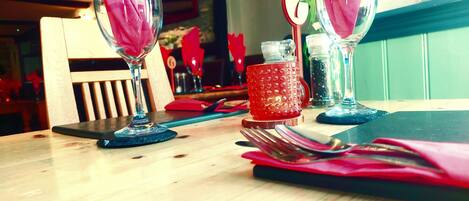 Une table à manger avec une tasse rouge, un verre et une serviette rose, et un menu accroché au mur.