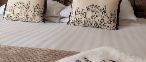 A hotel room with a bed, two pillows with floral designs, a headboard, and a framed picture on the wall.