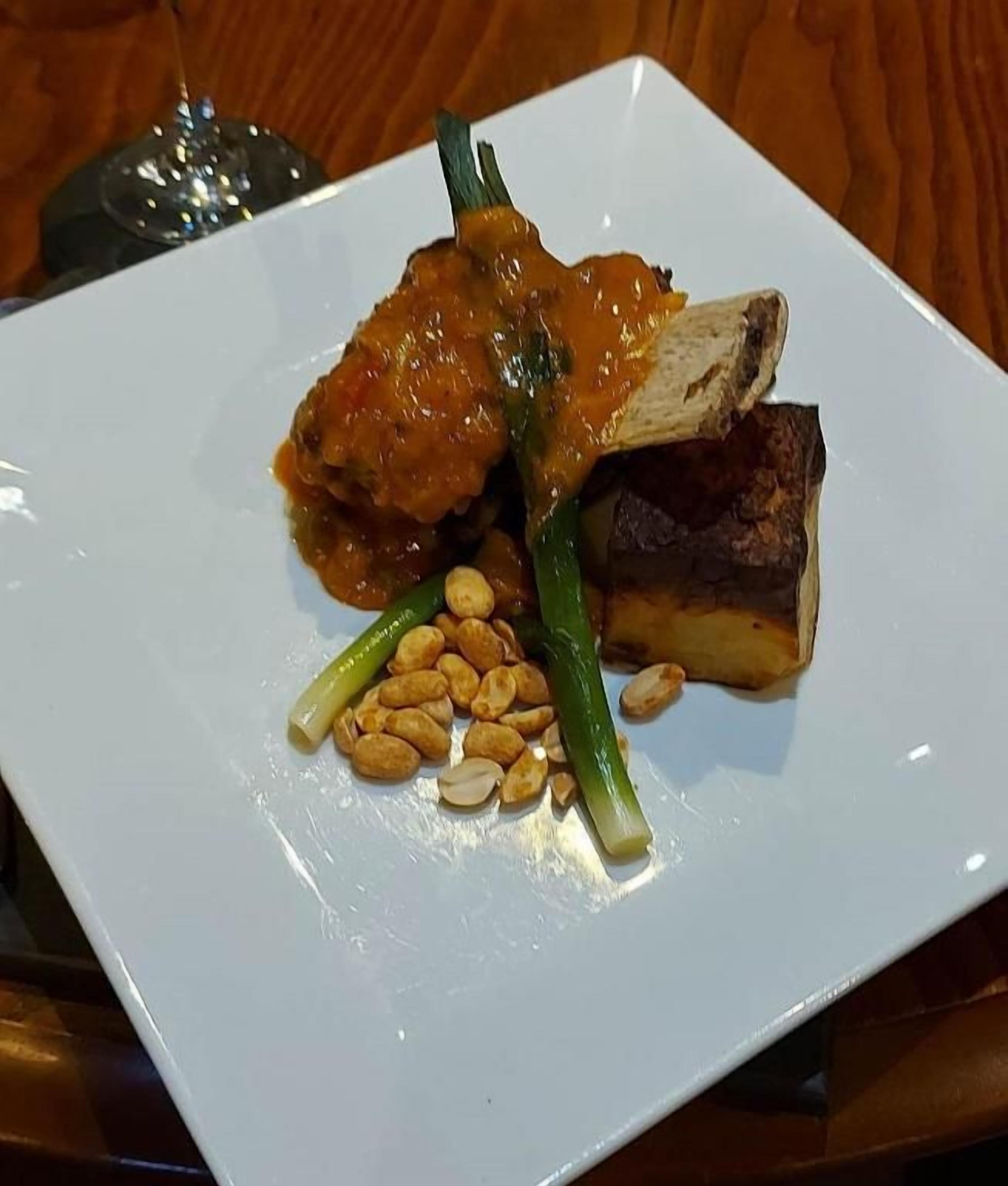 A white plate with a piece of meat, green vegetables, and peanuts.