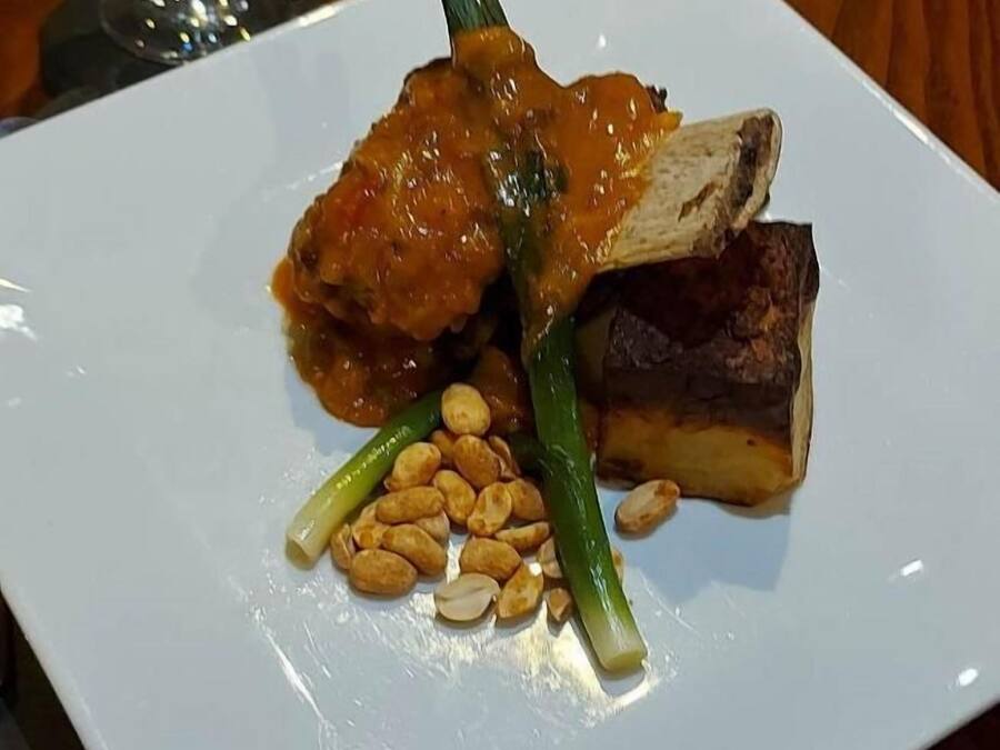 Ein weißer Teller mit Fleisch, grünen Gemüsesorten und Erdnüssen.