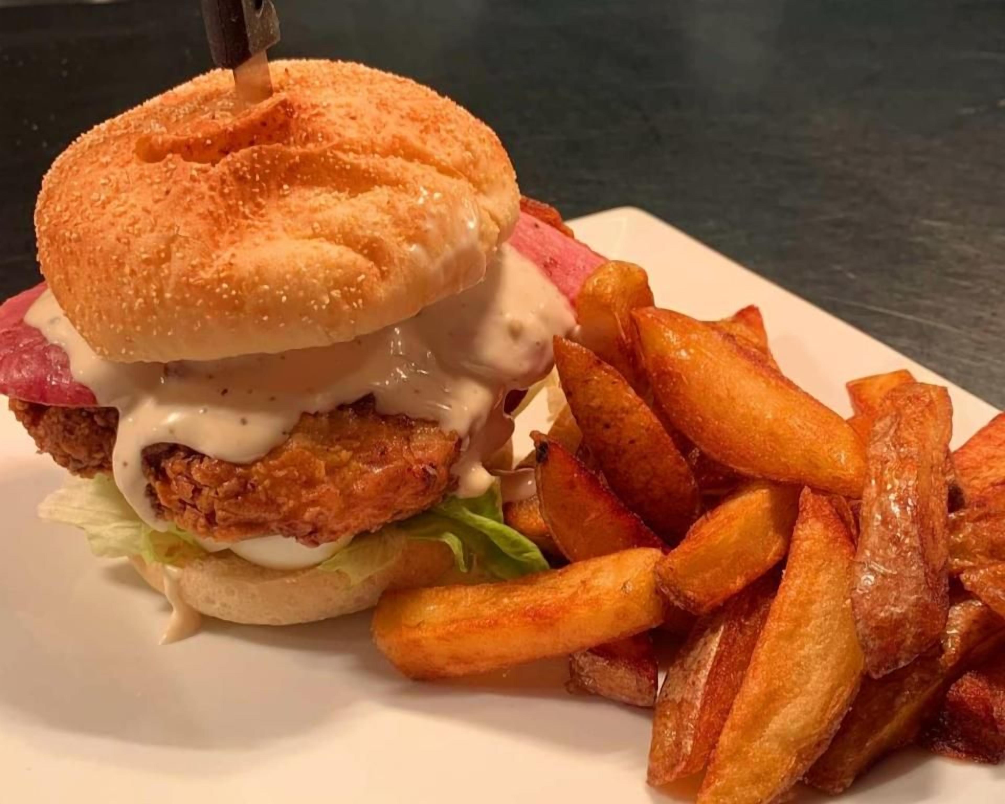 A sandwich with a bun, fried chicken, lettuce, and a creamy sauce, accompanied by a side of golden-brown fries.