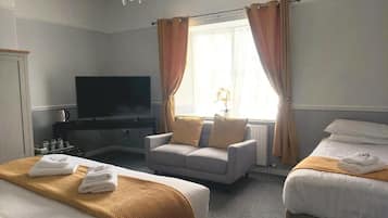 A hotel room with two beds, a sofa, a TV, and a window with curtains.