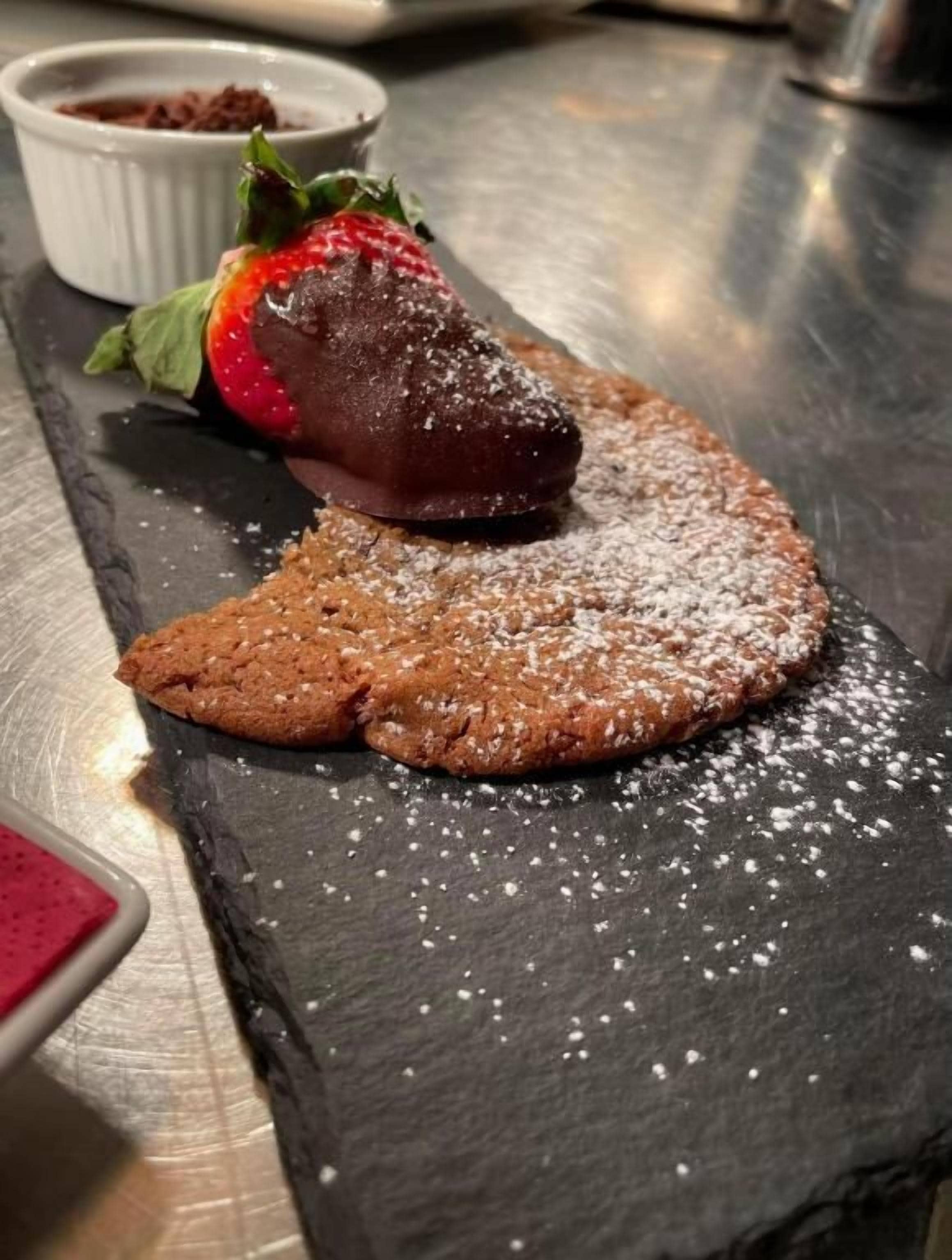 A dessert on a slate serving board with powdered sugar, a chocolate piece, and a strawberry.