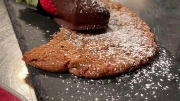 A dessert on a slate serving board with powdered sugar, a chocolate piece, and a strawberry.