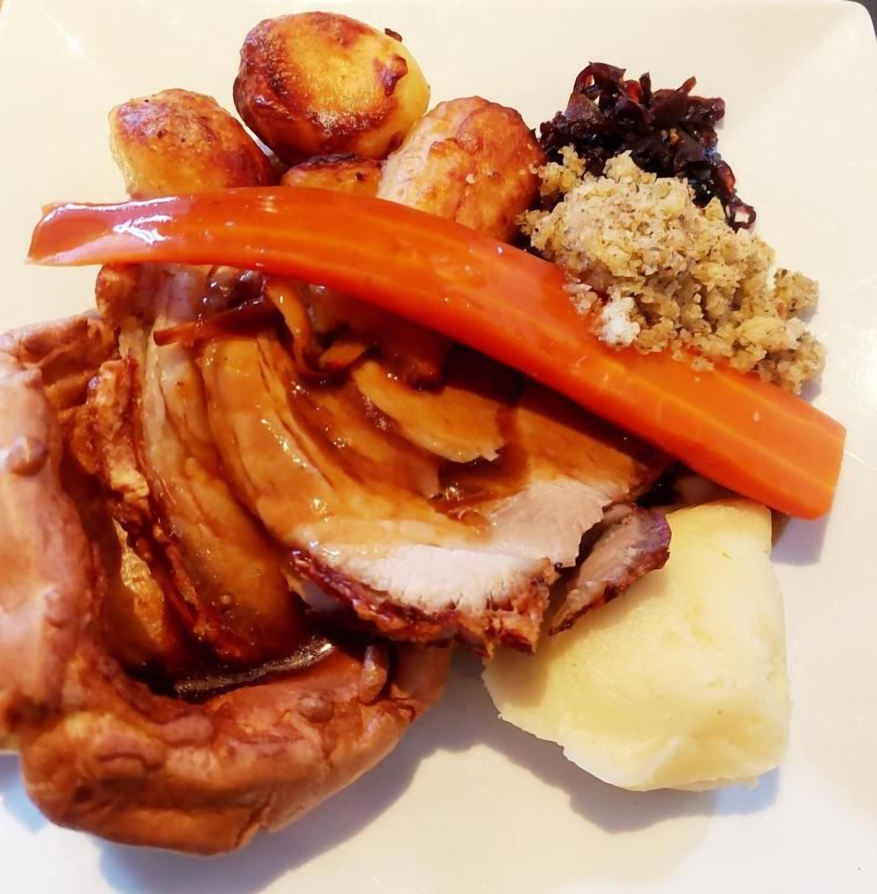 Une assiette de nourriture comprenant de la viande rôtie, des pommes de terre, des carottes et une portion de sauce.