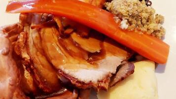 Une assiette de nourriture comprenant de la viande rôtie, des pommes de terre, des carottes et une portion de sauce.