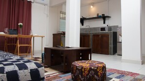 A compact living space with a bed, a small table, a desk, and a kitchenette.