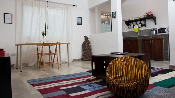 A living room with a dining table, chairs, a sofa, and a kitchen area with cabinets and appliances.