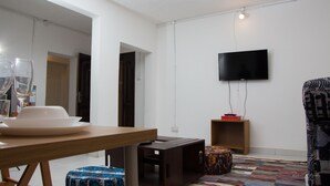 A modern living room with a wooden dining table, a television mounted on the wall, and a patterned rug on the floor.