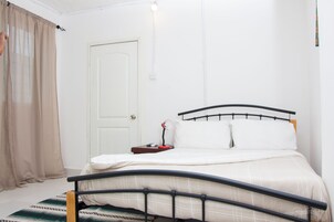 Un dormitorio con cama, mesita de noche, lámpara y puerta.