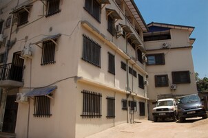 Un edificio de varios pisos con ventanas con rejas y unidades de aire acondicionado. Hay dos vehículos estacionados al frente.