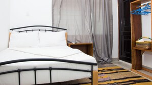 A bedroom with a bed, a wooden nightstand, a wardrobe, a patterned rug, and a door with a curtain.