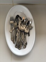 Un plato blanco con diversos utensilios de plata, incluyendo tenedores, cucharas y un cuchillo.