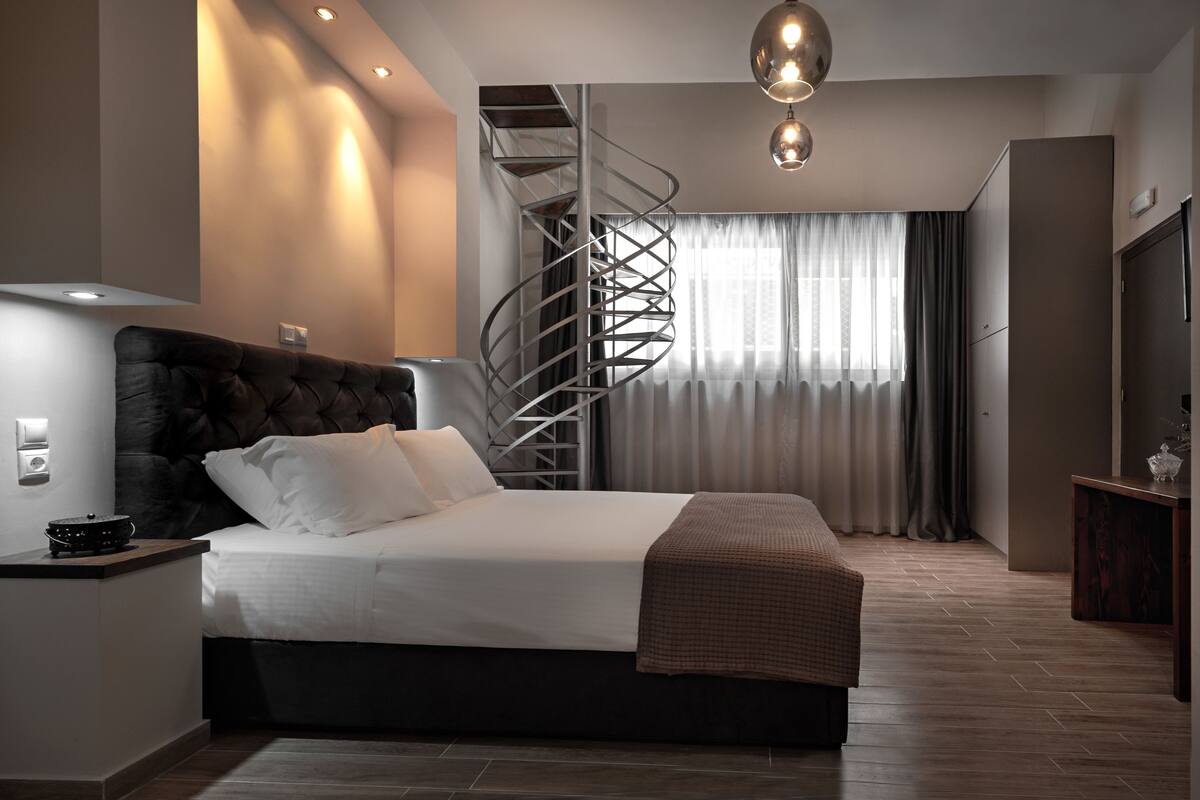Een moderne slaapkamer met een groot bed, een wenteltrap en uitzicht op het omliggende landschap.