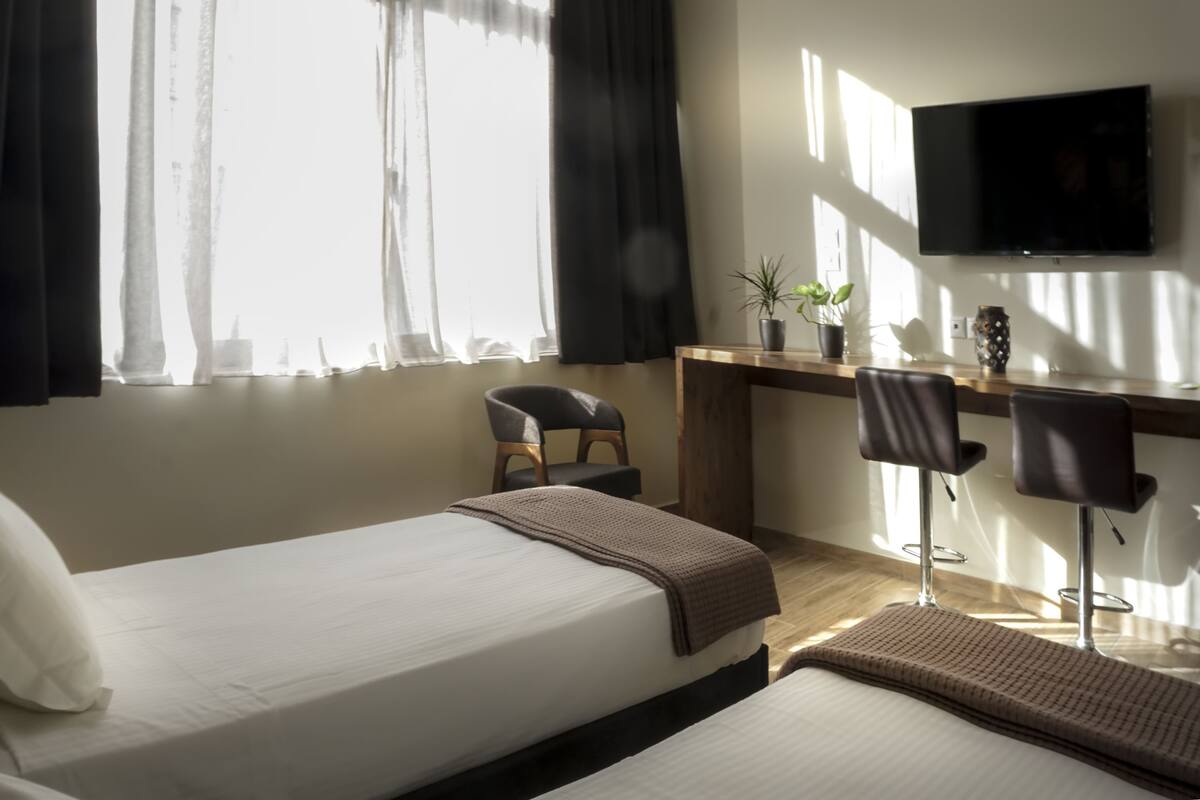 Een hotelkamer met een bed, een bureau, twee stoelen, een televisie en een raam met gordijnen.