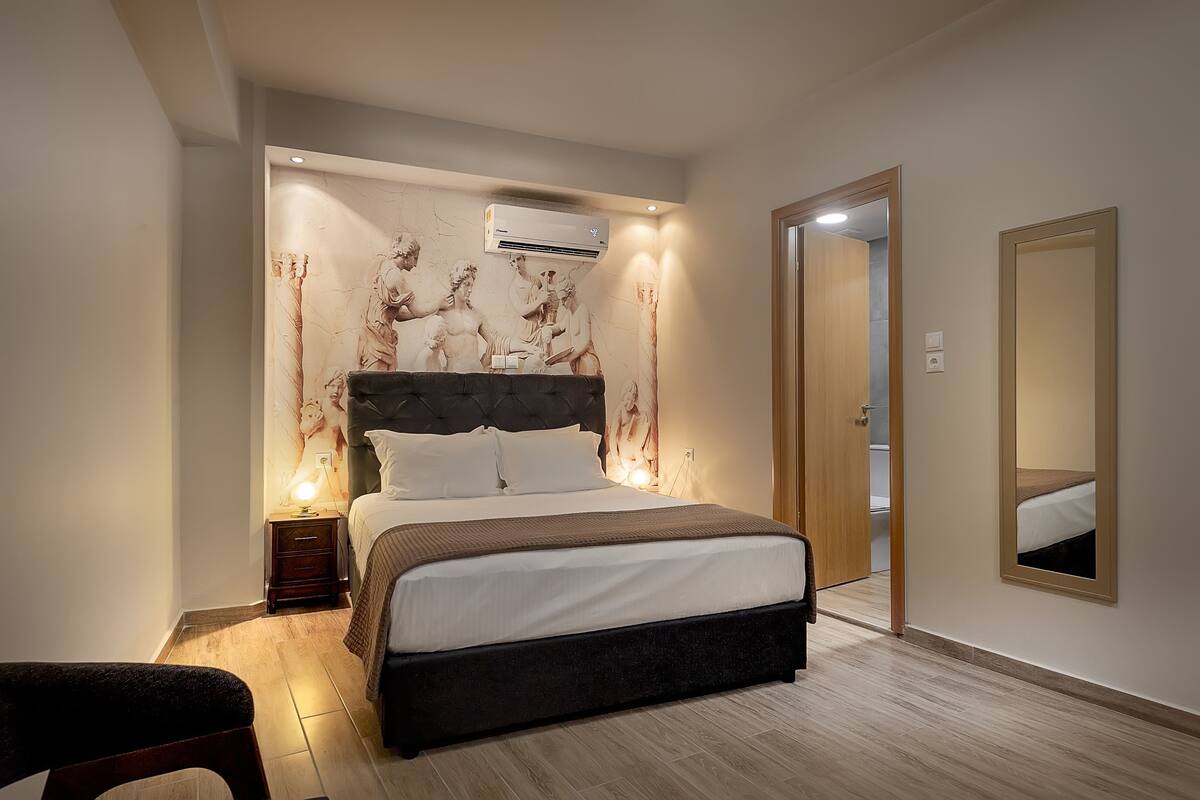 Een slaapkamer met een groot bed, een nachtkastje, een wandairconditioner en een spiegel aan de muur.