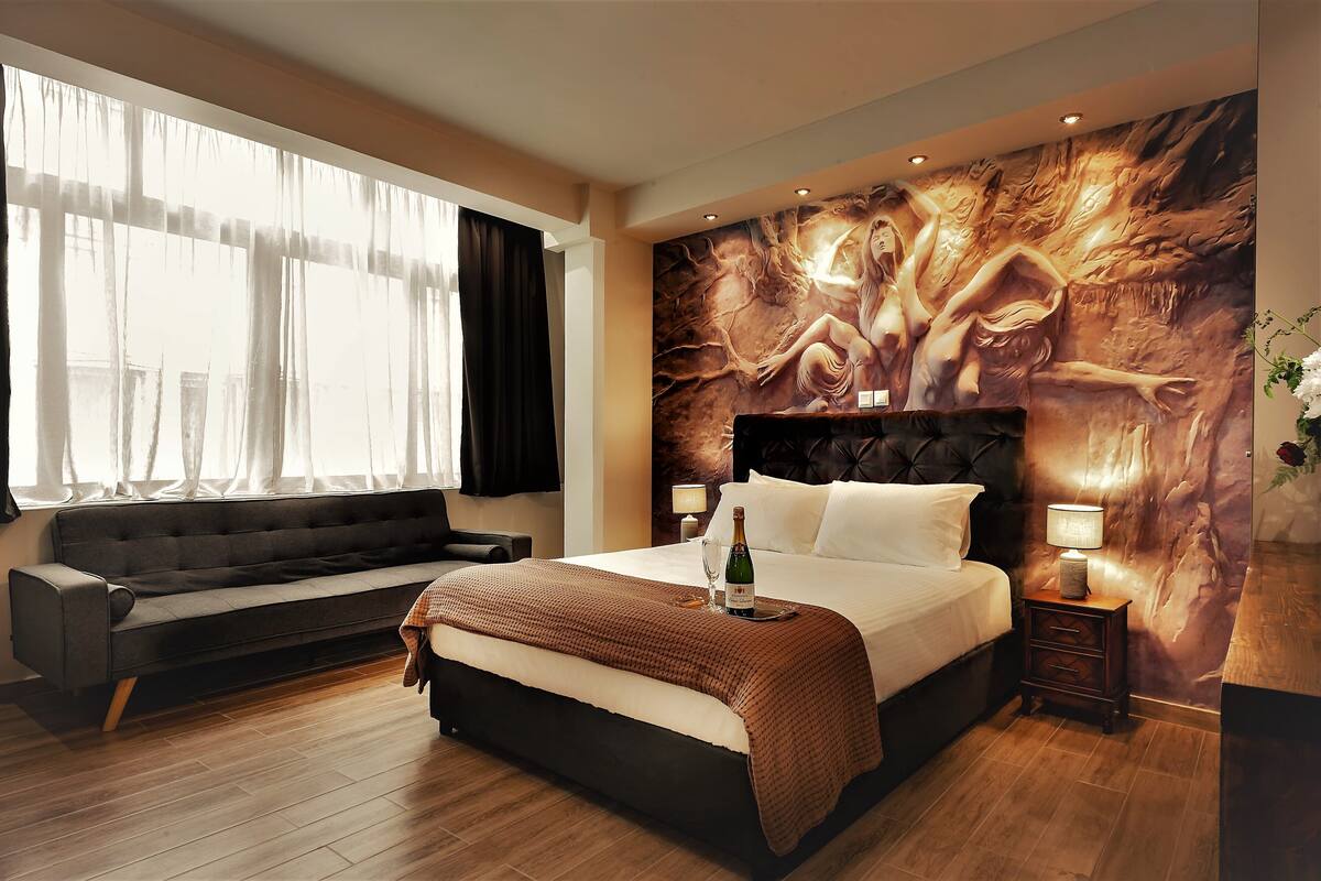 Een moderne hotelkamer met een groot bed, een bank, een muurschildering en een houten vloer.