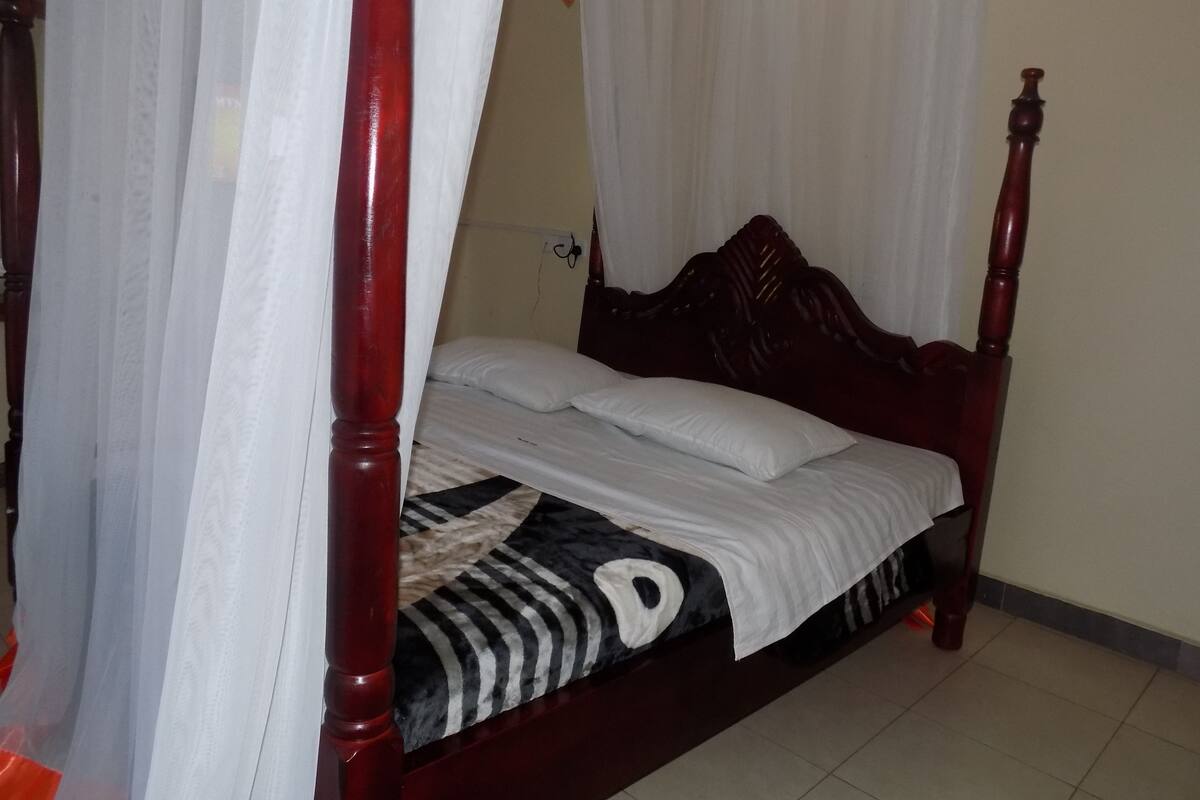 A bed with a wooden headboard, white bedding, and a black and white striped blanket.