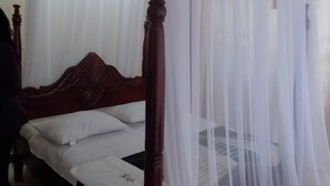 Un lit avec une tête de lit en bois, une literie blanche et une moustiquaire.