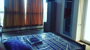 A room with a bed covered in plastic, a television on the wall, and a large window with curtains. - New Wave (Grigoleti)