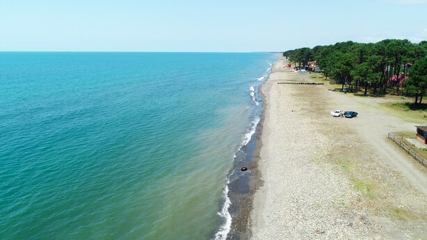 An aerial view of a beach with a pebbly shore, a clear blue sea, and a line of trees and buildings along the coastline. - New Wave (Grigoleti)