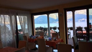 A dining area with tables and chairs, large windows with a view of a lake and mountains.