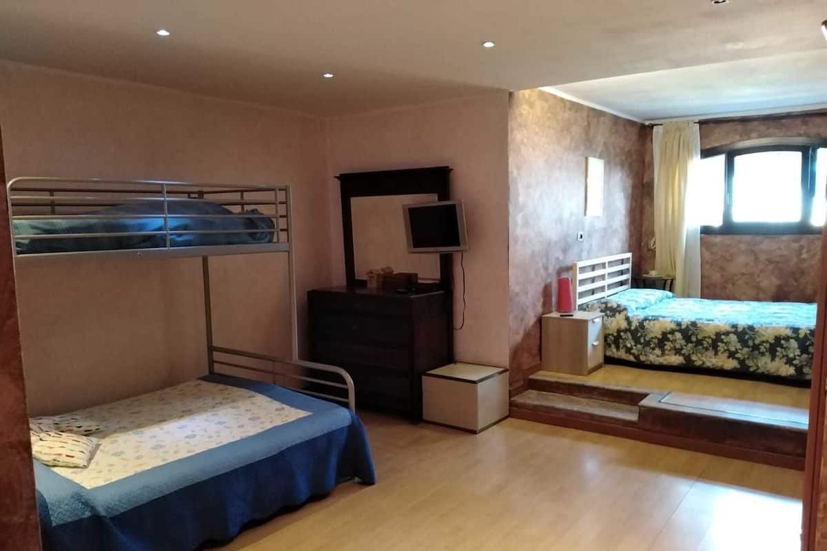 Um quarto com beliches, cômoda, televisão e janela com cortinas.