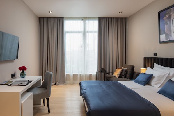 Habitación de hotel con cama, escritorio, silla, televisión y ventana con cortinas.