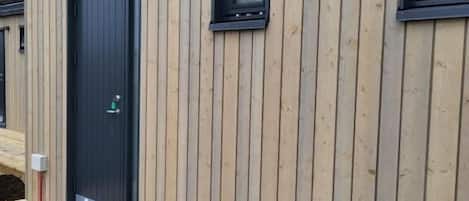 Een modern gebouw met verticale houten bekleding, een zwarte deur en twee kleine ramen.