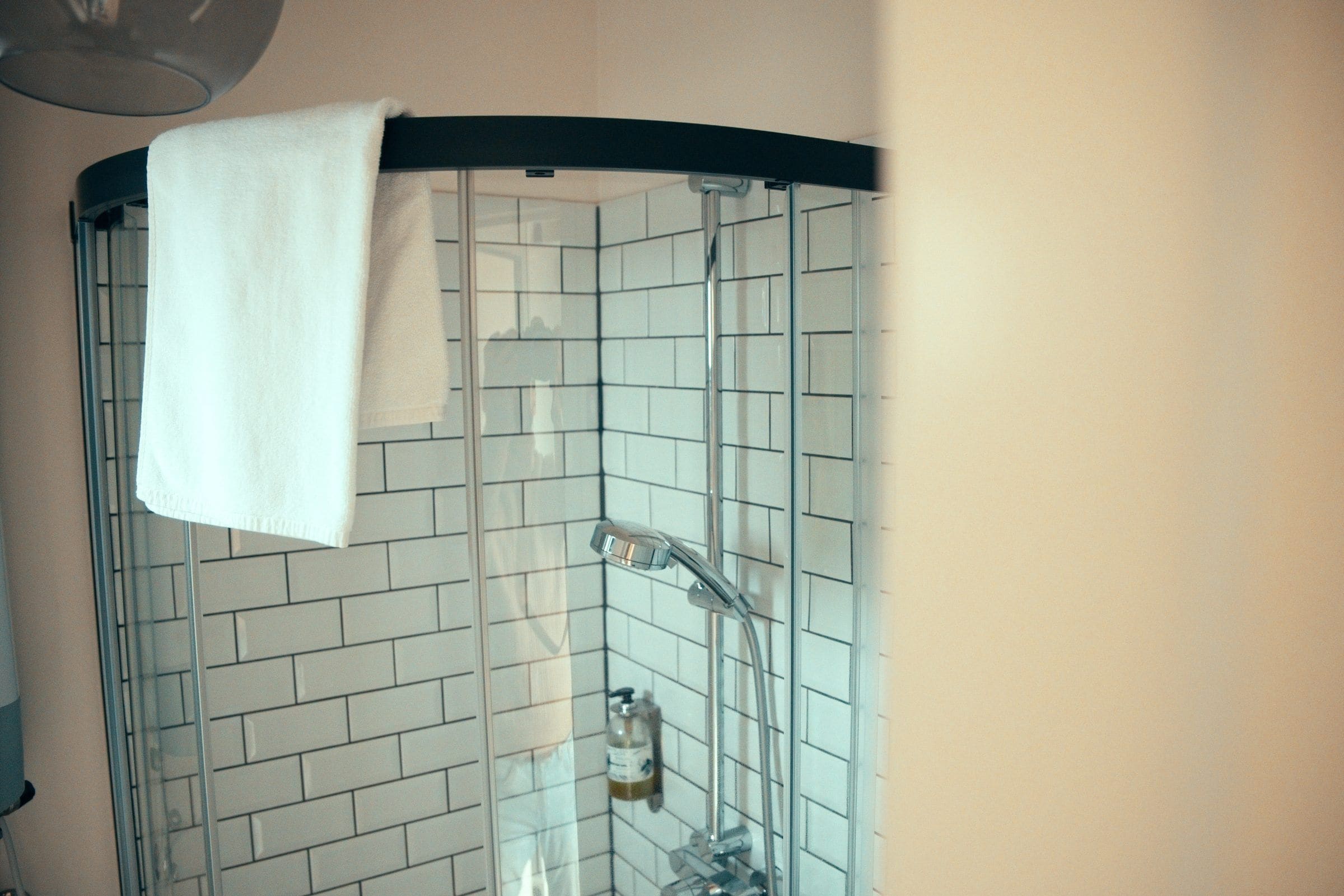 A corner shower with a white towel hanging on the door, tiled walls, and a visible showerhead.