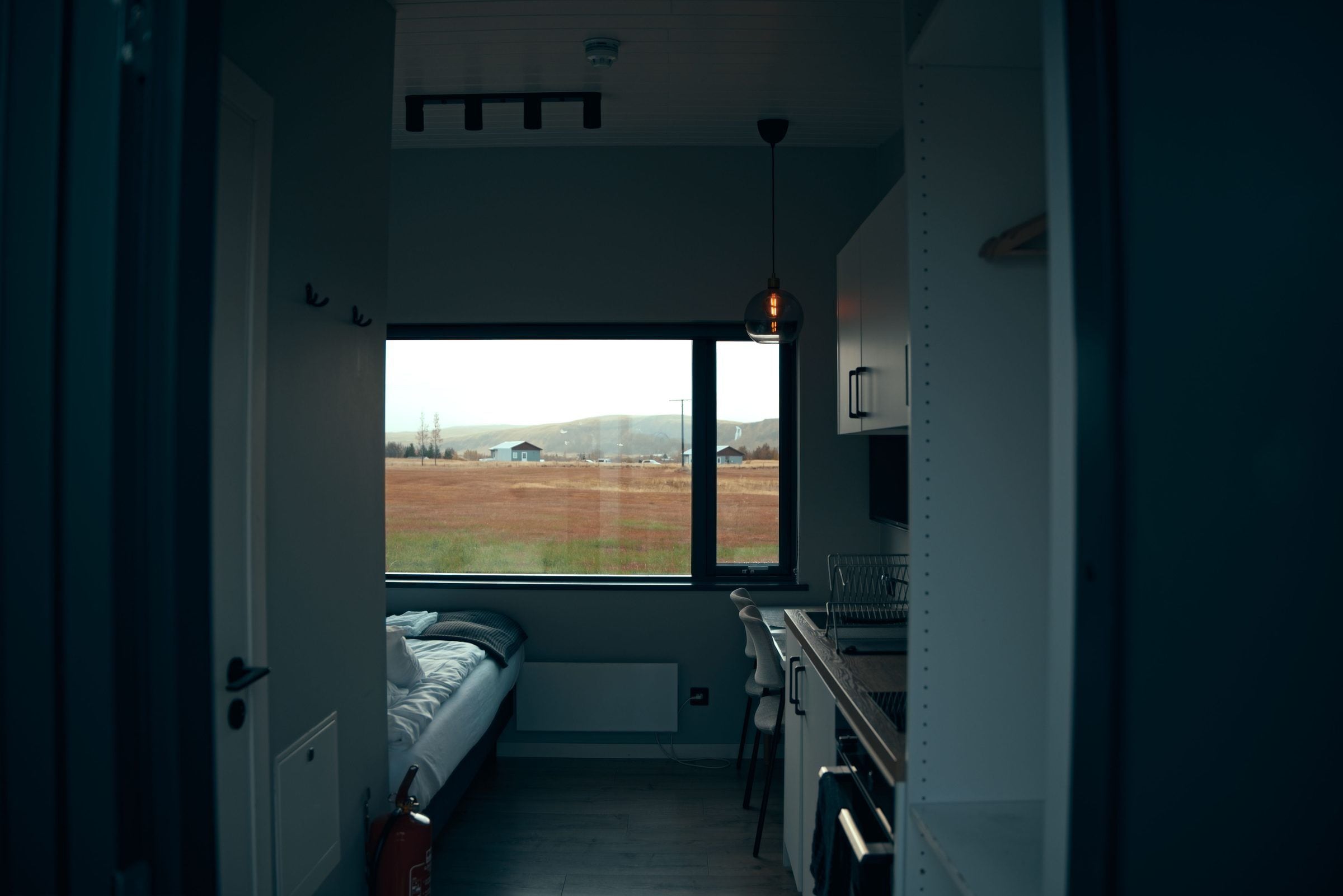 Una habitación pequeña con una cama, un ventanal y un rincón cocina.